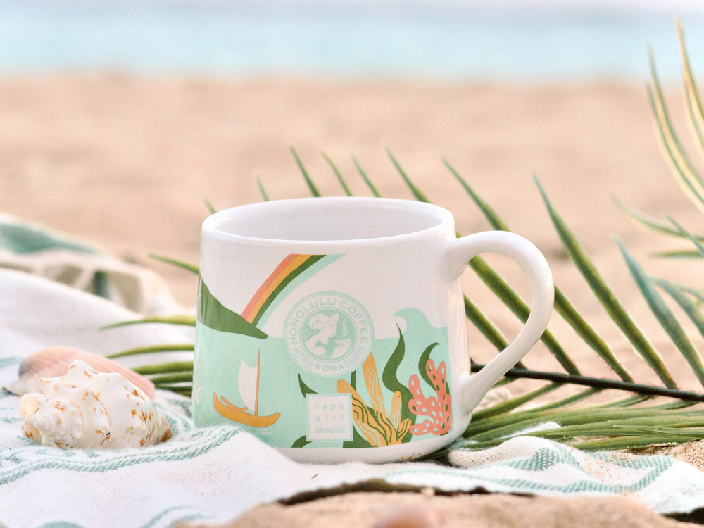 
                  
                    A mug on a beach towel with seashells on it.
                  
                