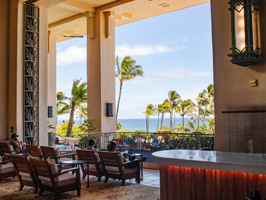 Indoor area with outdoor seating overlooking a scenic ocean view with palm trees.