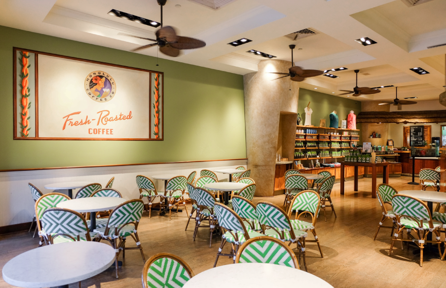 Coffee shop interior with tables, chairs, and a green wall with a coffee brand logo.