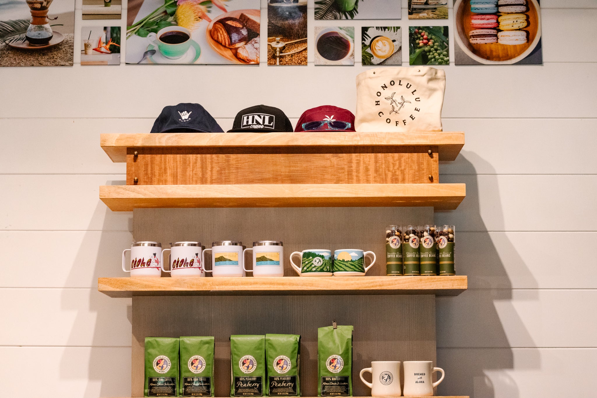 Wooden shelves with coffee-themed products including mugs, coffee bags, and branded hats against a wall with framed images.