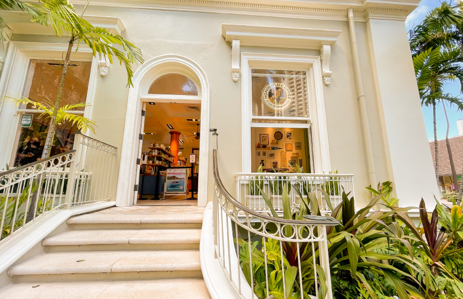 Staircase leading up to a white building with glass doors, surrounded by greenery.