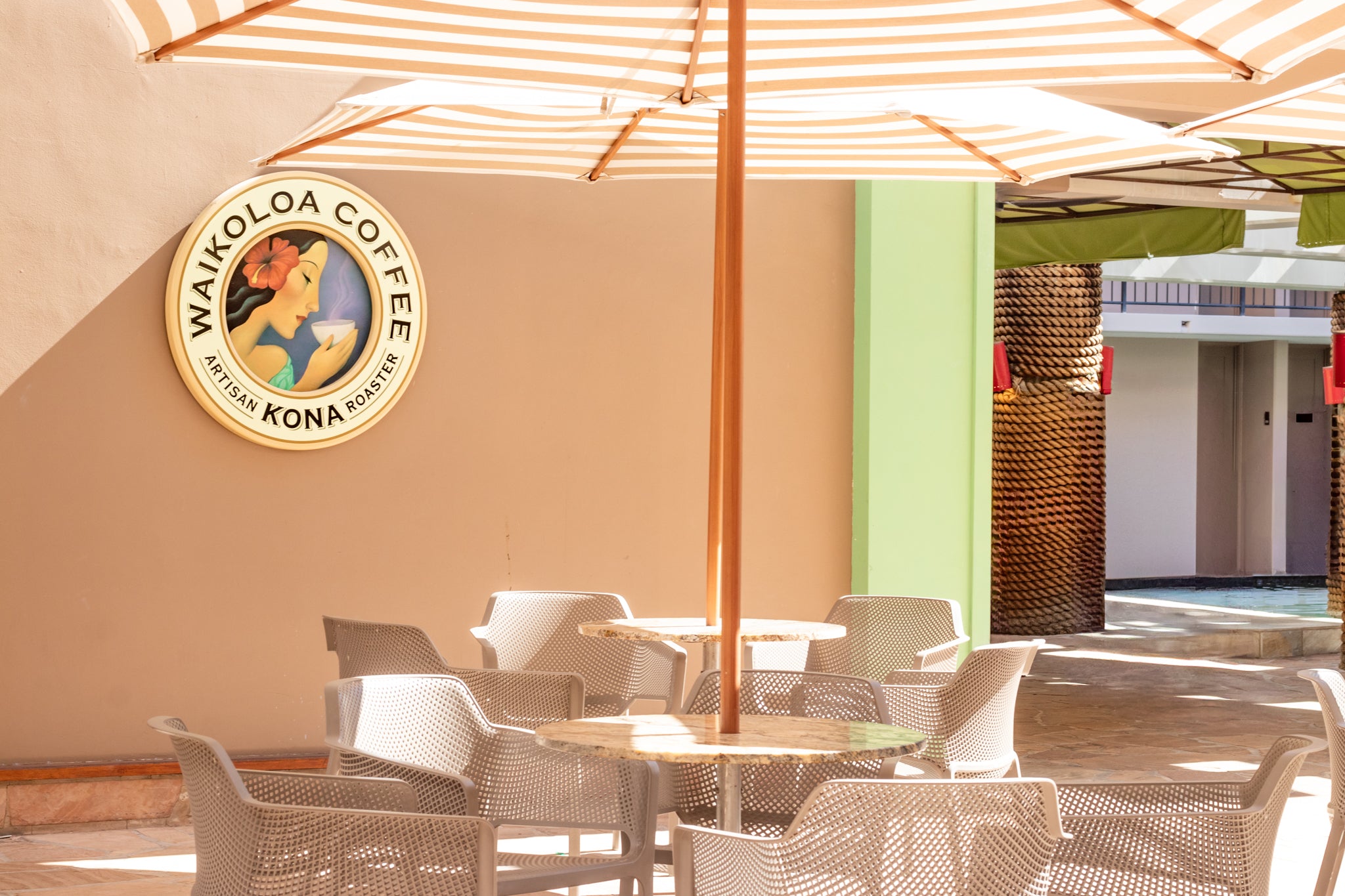 Outdoor seating area with 'Waikoloa Coffee' logo on a wall, featuring tables and chairs.