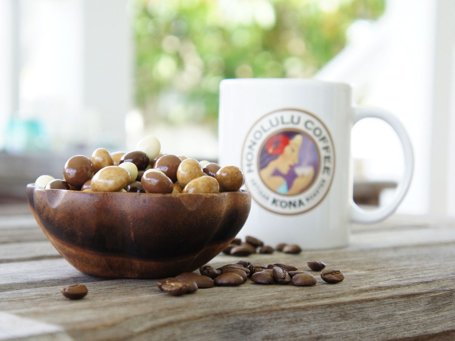 Mixed chocolate covered coffee beans sitting in a bowl next to a Honolulu Coffee Mug